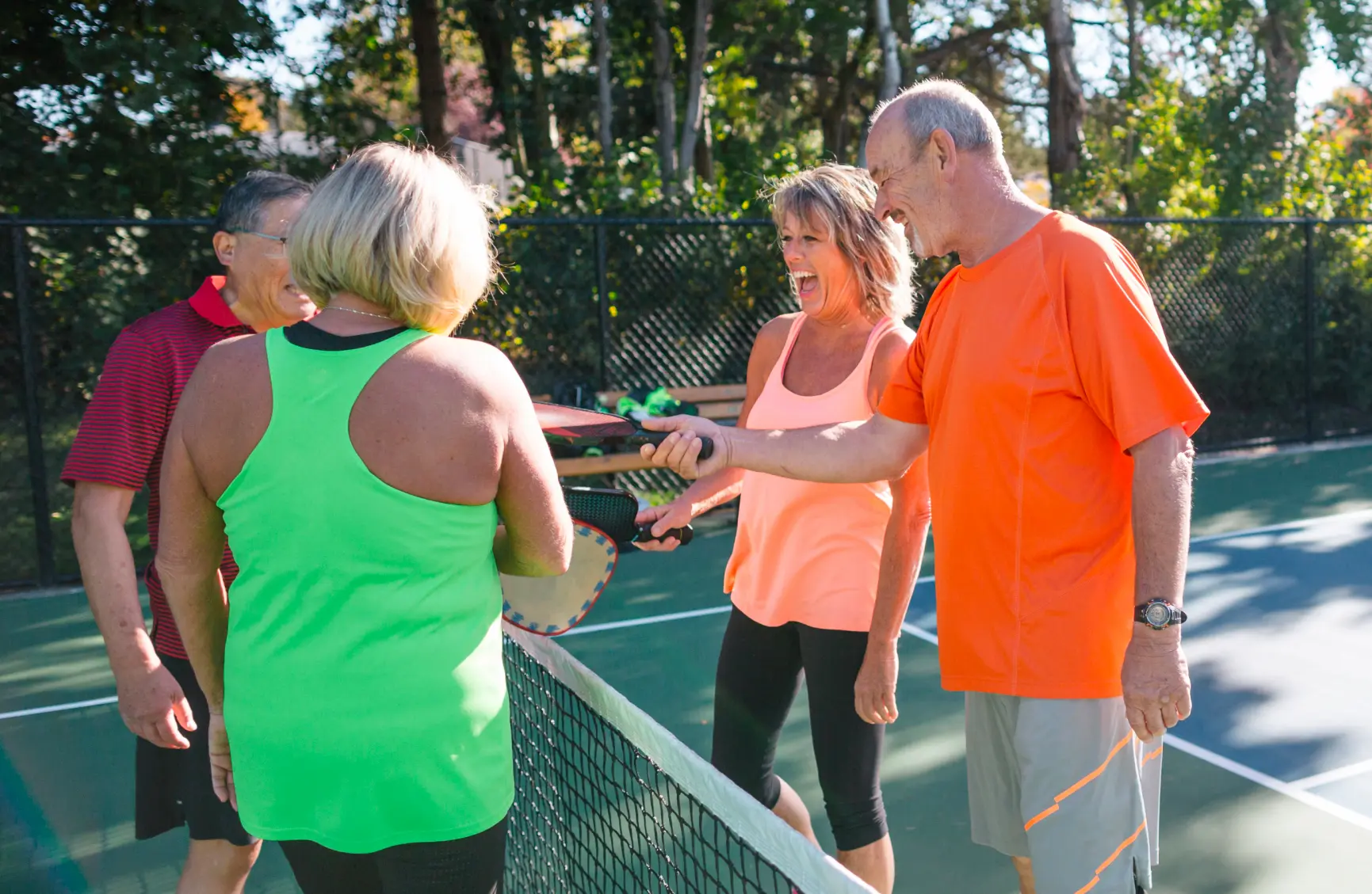 Four adults laughing over net on pickleball court | Rockwall Homes for Sale