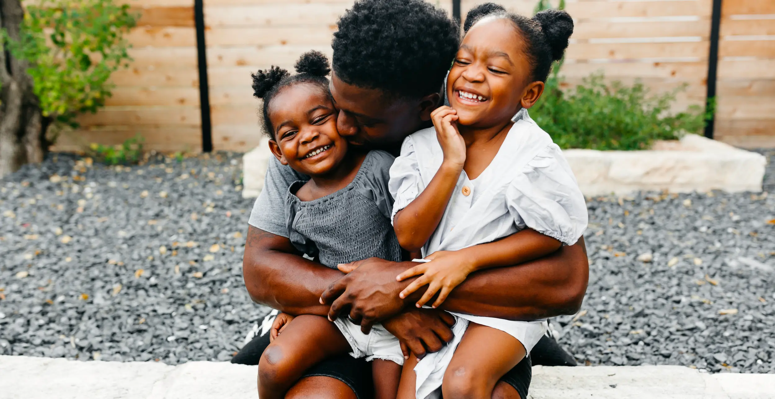 Man holding two small girls next to rock flower bed | Rockwall Homes for Sale