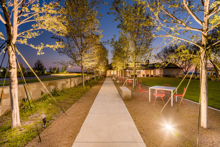 Tree-lined walkway illuminated at dusk with modern outdoor seating and landscaping at Hillstead.