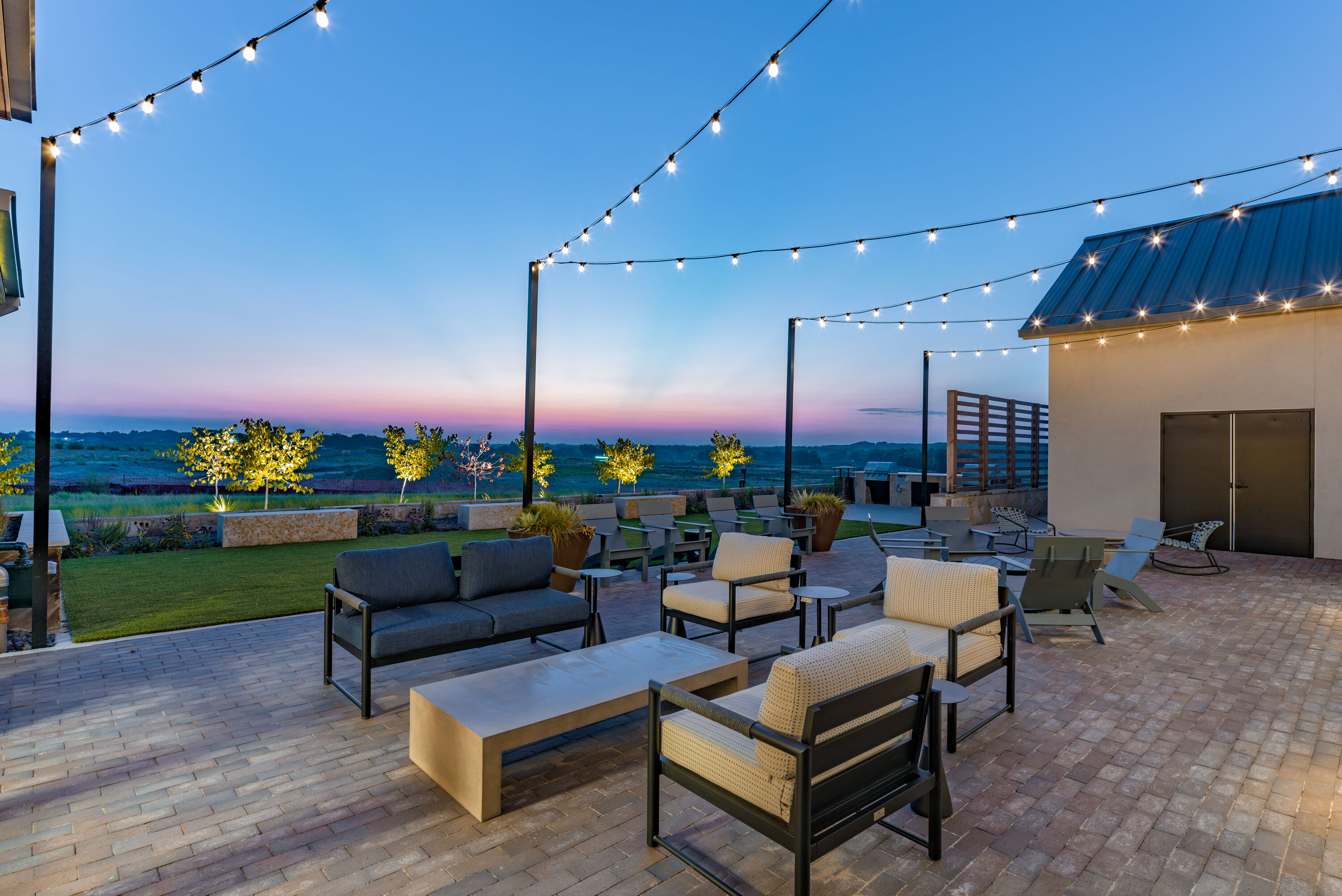 Outdoor patio with string lights, modern lounge seating, and sunset views over the landscape at the Hillstead clubhouse