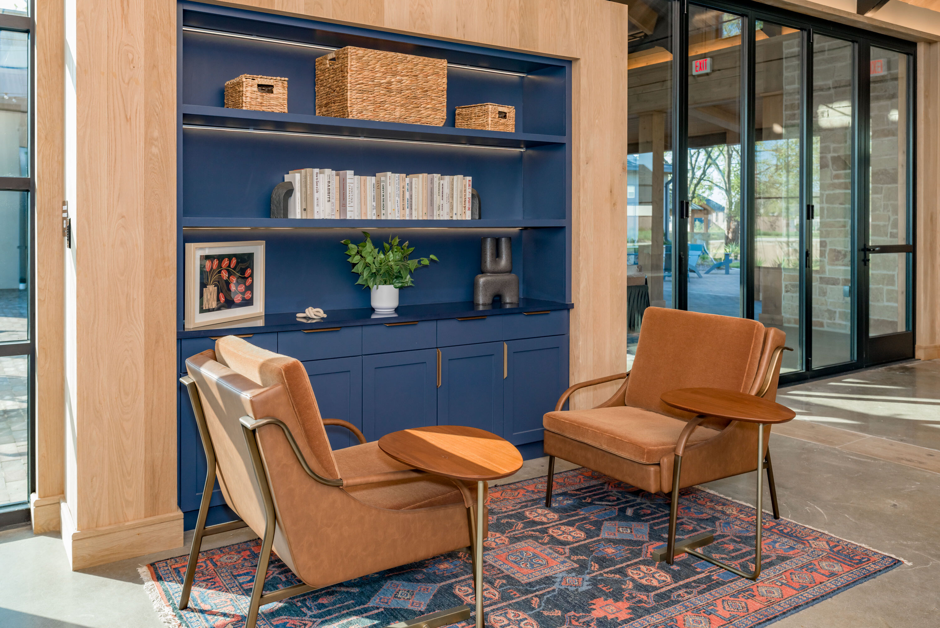 Modern lounge area with leather chairs, wooden tables, and a navy built-in bookshelf at the Hillstead clubhouse.