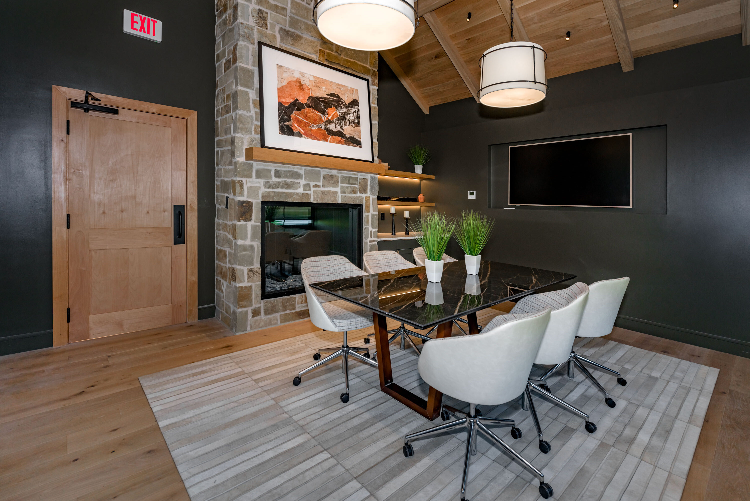 Modern meeting room with a stone fireplace, glass table, and contemporary lighting at the Hillstead clubhouse.
