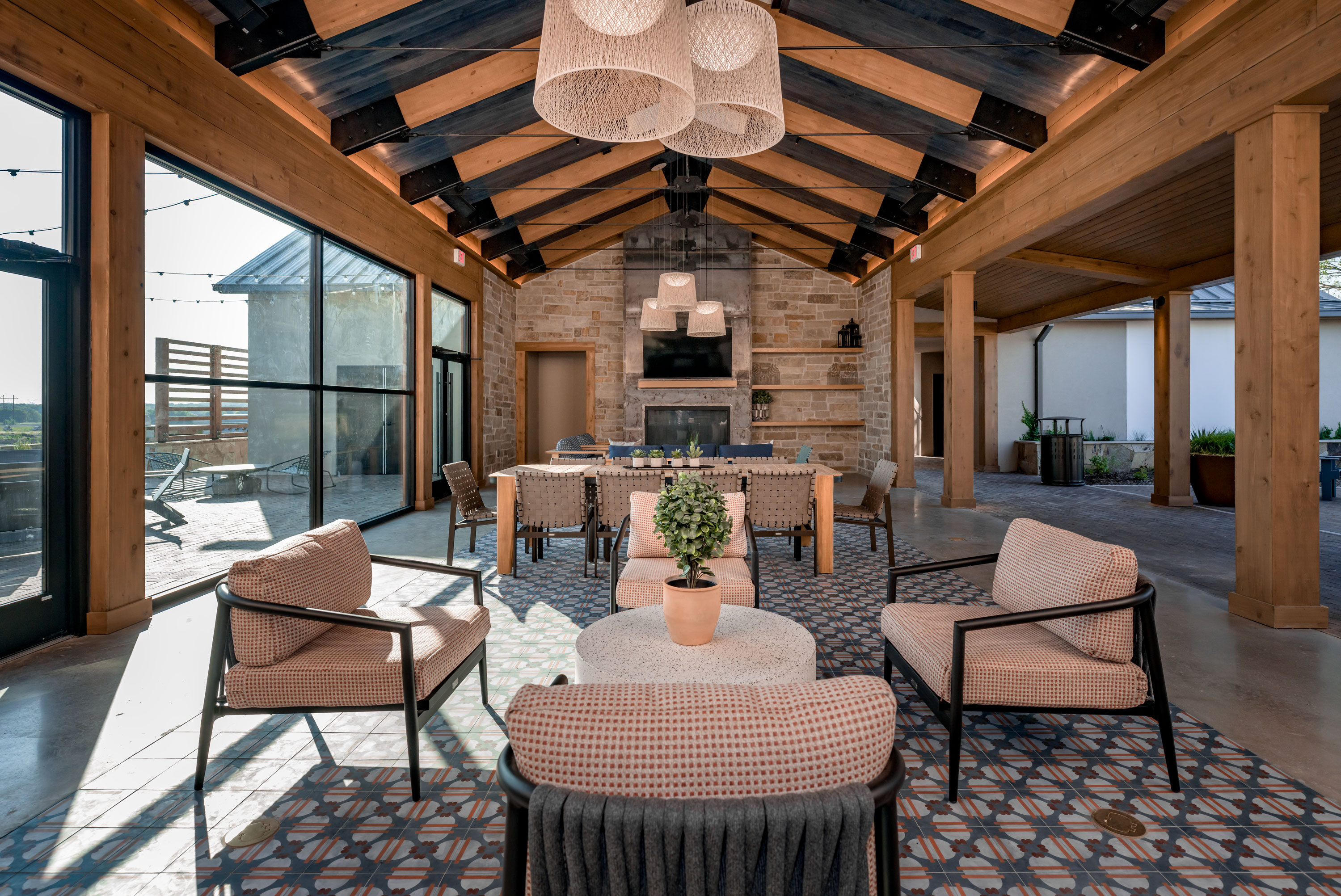 Spacious covered lounge with modern seating, patterned tile flooring, and a stone fireplace at the Hillstead clubhouse.
