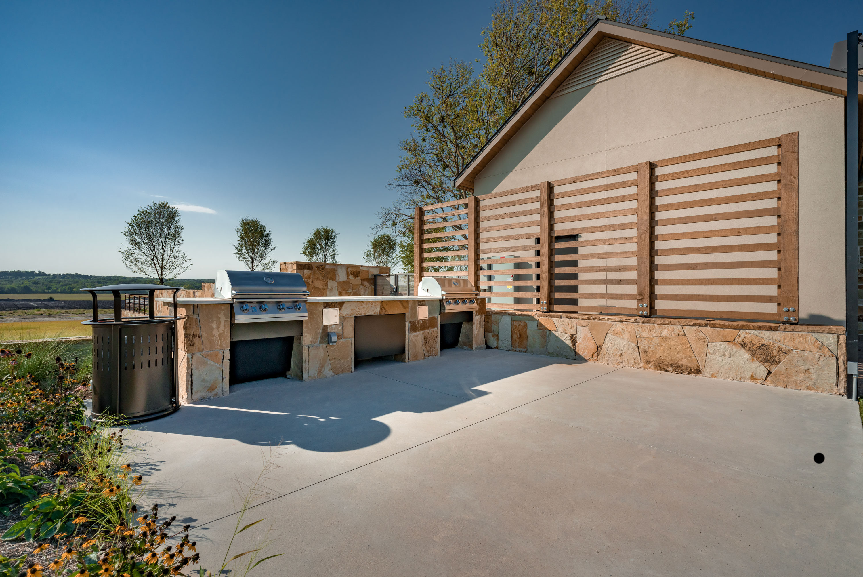 Outdoor grilling area with built-in stone barbecues and modern wood privacy panels.