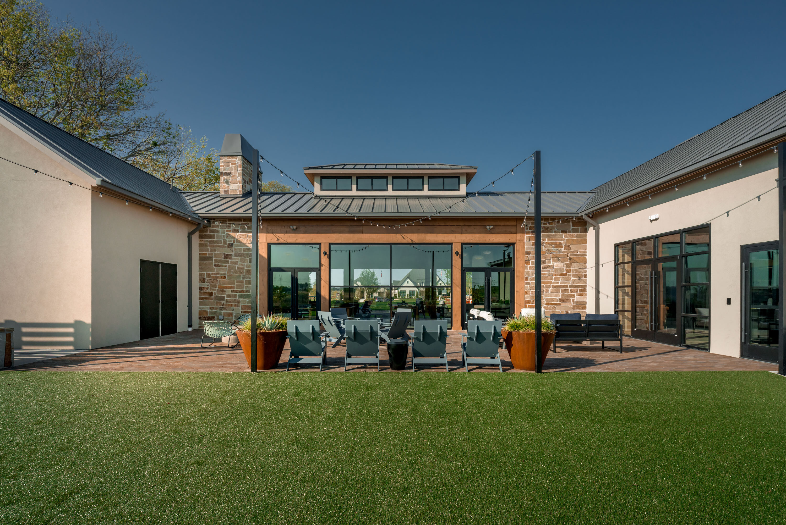 Modern clubhouse exterior with patio seating, string lights, and lawn area at Hillstead.
