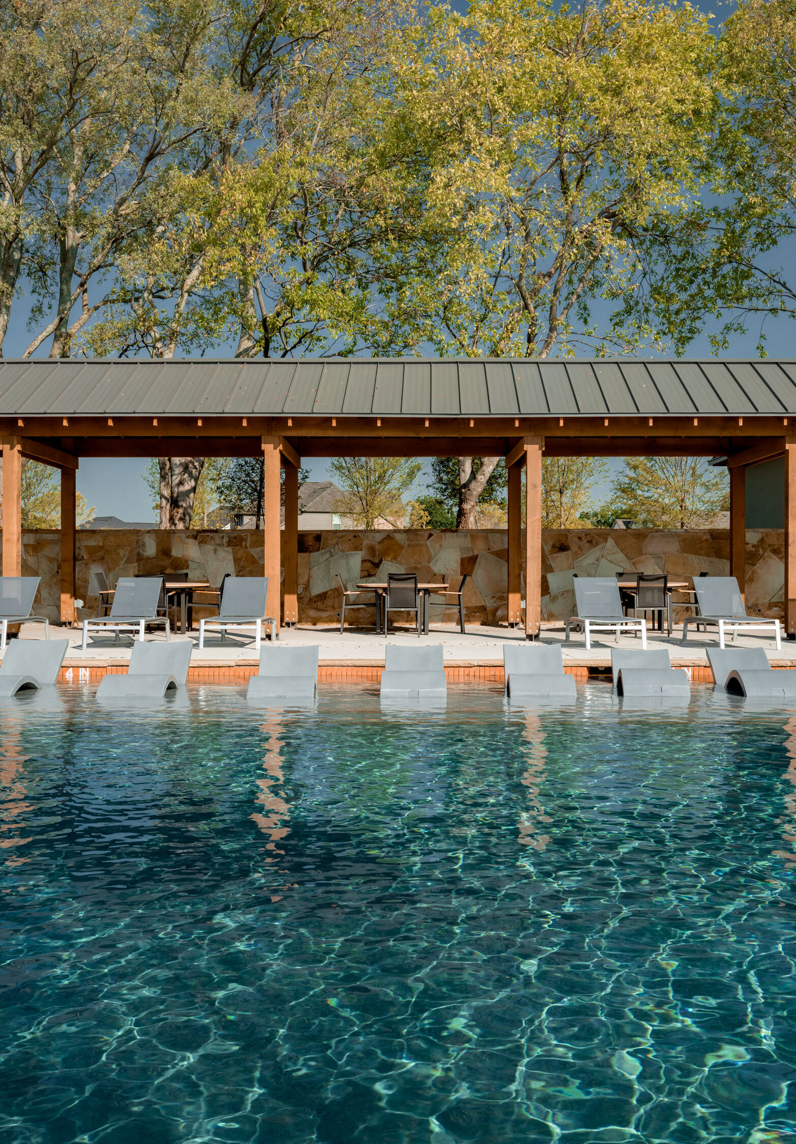 Resort-style swimming pool with in-water lounge chairs and shaded cabana seating surrounded by trees at Hillstead.