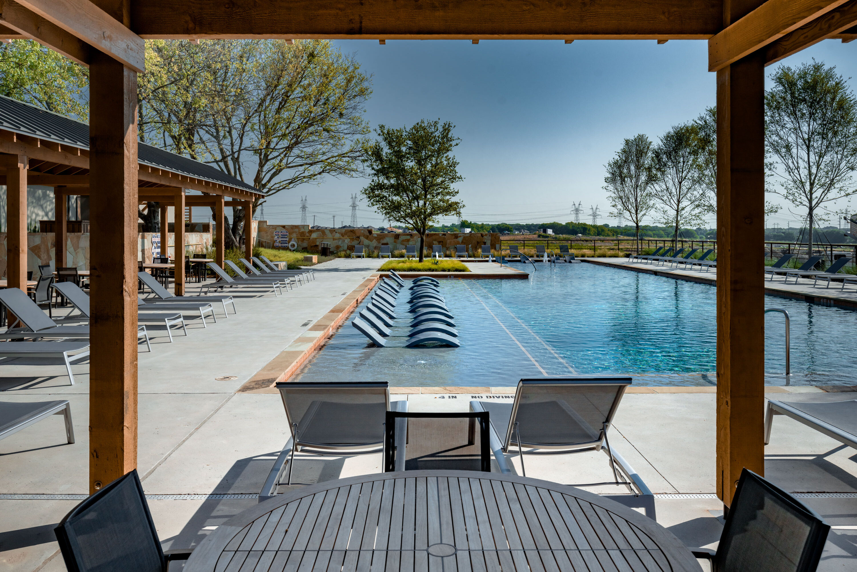 View of resort-style pool with in-water loungers, shaded cabanas, and seating areas under wooden pergolas at Hillstead.