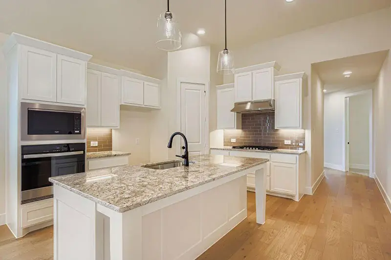 American Legend kitchen with a granite center island, white shaker cabinets, and a grey subway tile backsplash